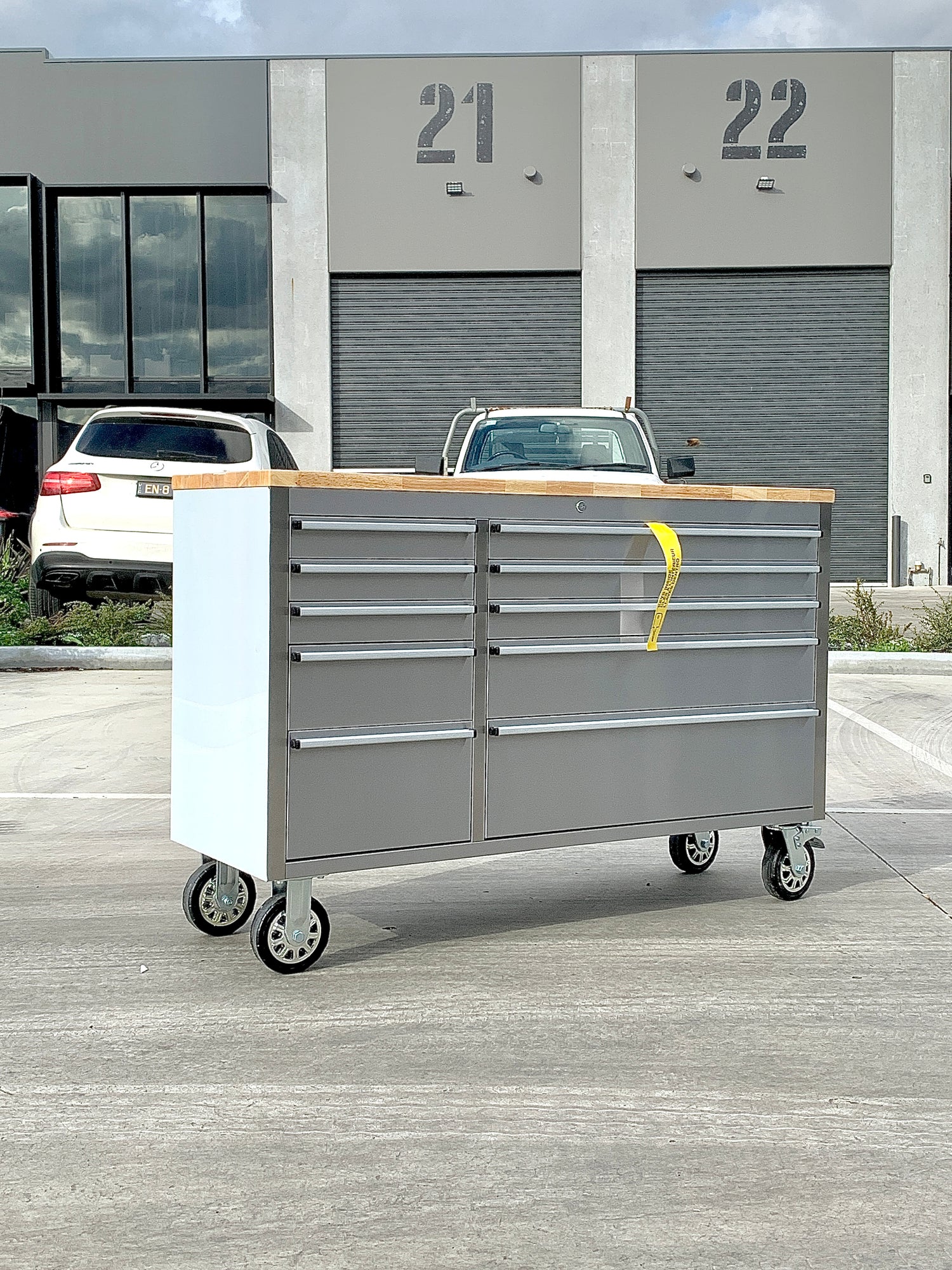 Silver rolling tool cabinet with multiple drawers and a wooden top, set outdoors in an industrial setting